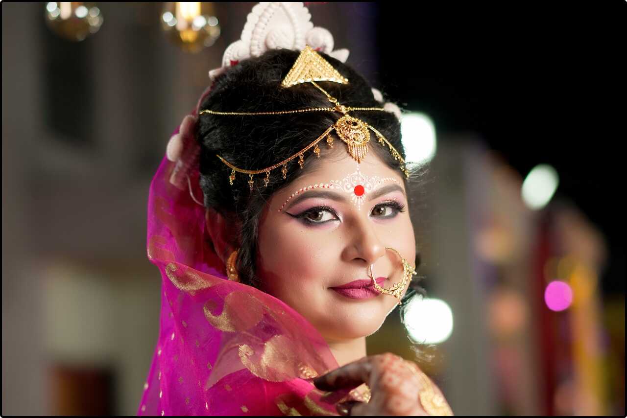 Traditional Bengali bride with a mukut headpiece and gold ornaments, posing gracefully for a wedding portrait.